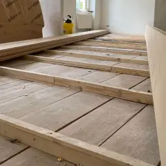 Holzbalken werden auf einem alten Holzboden verlegt, um ihn für neue Bodenplatten vorzubereiten. So kann man den Boden ausgleichen ohne Ausgleichsmasse.