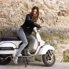Joven con chaqueta de cuero y jeans sobre una scooter blanca, lista para el mantenimiento de su scooter 125.