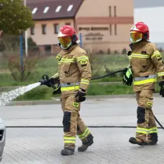 Dwóch strażaków w akcji. Jeden z nich kieruje strumień wody na pojazd. Zastanawiasz się, ile zarabia strażak?