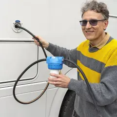 Un homme utilise un filtre à eau pour le remplissage d'eau de son camping-car. Une astuce pratique pour une eau pure en voyage.