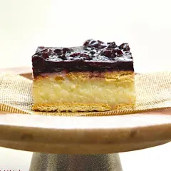 Pyszne ciasto z kaszy mannej bez pieczenia z polewą wiśniową, podane na drewnianym talerzyku.