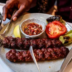 Dwa soczyste, grillowane kebaby na talerzu z ryżem, pomidorem, papryką i sosem. Tak wygląda pyszny kebab!