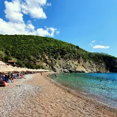 Słoneczne plaże w Budvie, z kamyczkami i piaskiem, otoczone zielonymi wzgórzami. Krystalicznie czysta woda Adriatyku zaprasza do kąpieli.