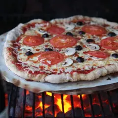En härlig pizza på grillen med tomater, champinjoner och oliver. Glödande kol under ger en perfekt krispig botten.