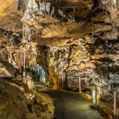 Interior de cuevas cerca de Madrid, con estalactitas y estalagmitas iluminadas, y un sendero metálico para visitantes.