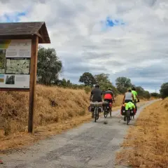 Ciclistas disfrutan de una ruta cicloturista por la Vía Verde de Monfragüe, con un cartel informativo al inicio del camino.