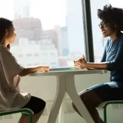Deux femmes discutent à une table, l'une semble faire une demande d'entretien avec son directeur.