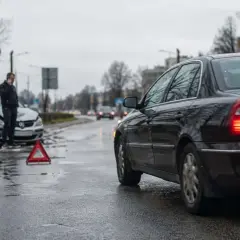 Wypadek drogowy. Mężczyzna rozmawia przez telefon obok uszkodzonego samochodu. Trójkąt ostrzegawczy na drodze. Sprawa dla ubezpieczyciela, regres ubezpieczeniowy.
