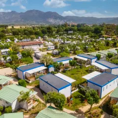 Un complejo de bungalows y caravanas para ir de camping, con montañas al fondo y un cielo azul.