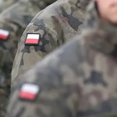 Żołnierze w mundurach moro, z polskimi flagami na ramionach, stoją w deszczu. Kategoria b wojsko.