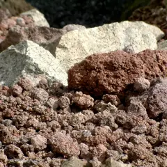Głęboki zbliżenie na wulkaniczny **tuff** – drobne, porowate kamienie w odcieniach czerwieni i szarości, tworzące surowy krajobraz.