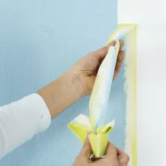 Händer drar bort maskeringstejp vid målning. Tejpen har färgfläckar från det blå och gula som målats.