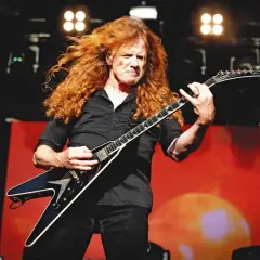 Dave Mustaine z burzą rudych włosów gra na gitarze w kształcie skrzydła.