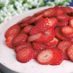 En läcker jordgubbsmousse tårta, toppad med färska jordgubbsskivor och vita blommor i bakgrunden.