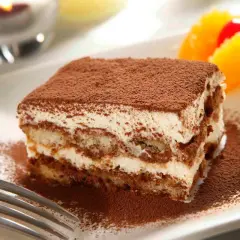 Un délicieux tiramisu Kinder Bueno, saupoudré de cacao, avec des fruits en arrière-plan.