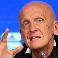 Pier Luigi Collina, znany sędzia piłkarski, przemawia do mikrofonu, gestykulując prawą ręką.