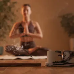 Kobieta w pozycji medytacyjnej, z kadzidełkiem w dymie. Badania naukowe potwierdzają korzyści płynące z medytacji dla zdrowia psychicznego i fizycznego.