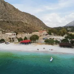 Kamienna plaża i turkusowe morze w Grecji kontynentalnej. W tle kamienne domy i góry. Idealne miejsce na wakacje.