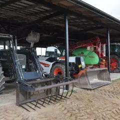 Ciągniki i maszyny rolnicze pod zadaszeniem. Widać zielony Fendt z ładowaczem, biały Bobcat, zielony opryskiwacz i ciągnik z rozsiewaczem. To wszystko w budynku gospodarczym bez zgłoszenia.