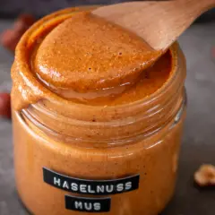 Cremiges Haselnussmus im Glas, bereit für leckere Rezepte mit Haselnussmus. Ein Holzlöffel schöpft die köstliche Masse.