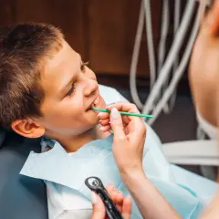 Chłopiec uśmiecha się, gdy dentystka bada jego zęby. Nie martwi się wypadaniem zębów, bo wie, że to naturalny proces.