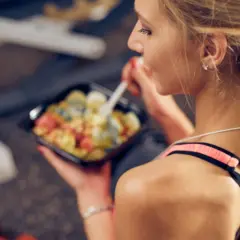 Junge Frau isst nach dem Sport eine gesunde Mahlzeit aus einer Plastikschale.