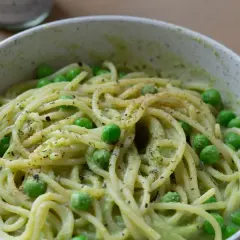 Eine Schüssel mit gesunden Nudeln, garniert mit Erbsen und Kräutern, serviert in einer cremigen grünen Sauce.