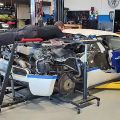 Mekaniker ligger på en rullande bänk och arbetar med en bilmotor. Frågan om hur ofta ska man byta olja i bilen är relevant för att hålla motorn i toppskick.