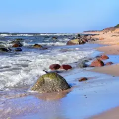 Kamienista plaża nad Bałtykiem, fale rozbijają się o brzeg. Dębina atrakcje to spacer po klifie i podziwianie widoków.