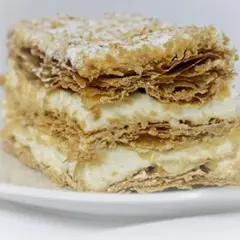 Deliciosa porción de costrada de Soria, con capas crujientes de hojaldre y crema suave, espolvoreada con azúcar glas.