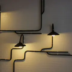 Nowoczesne lampy z czarnymi kloszami tworzą geometryczny wzór na białej ceglanej ścianie, zapewniając subtelne podświetlenie ściany od dołu.