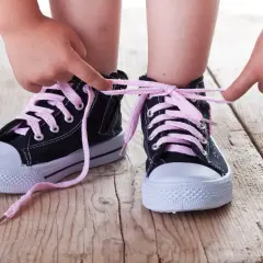 Dziecko uczy się, jak zawiązać buty. Instrukcja krok po kroku: maluch wiąże różowe sznurówki w czarnych trampkach.
