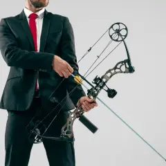Mężczyzna w garniturze i czerwonym krawacie trzyma łuk rambo z zamontowaną strzałą.