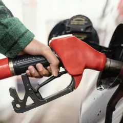 Dłoń trzymająca czerwoną dyszę paliwa przy samochodzie. Zastanawiasz się, jakie paliwo do zagęszczarki? To pytanie często pojawia się przy pracach budowlanych.