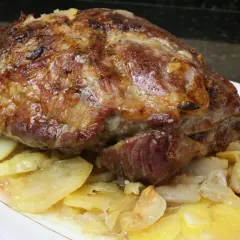 Cabezada de cerdo asada, jugosa y dorada, servida sobre patatas y cebolla caramelizada en un plato blanco.