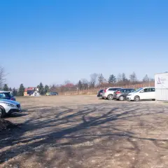Parking przy Kopcu Piłsudskiego. Kilka samochodów stoi na placu, w tle budynki i drzewa. Na kontenerze widoczny napis "SPRZEDAŻ WINA".