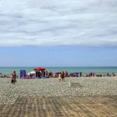 Tłum ludzi wypoczywa na kamienistej plaży w Batumi. Kolorowe parasole chronią przed słońcem.