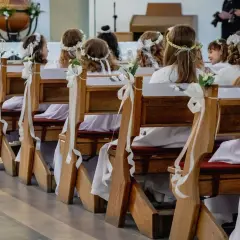 Dzieci w białych strojach i wiankach siedzą w kościele, czekając na uroczystość. Zastanawiasz się, ile trwa komunia?