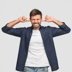 Mężczyzna zatyka uszy, cierpiąc z powodu hałasu. Dowiedz się, gdzie zgłosić uciążliwy hałas i odzyskać spokój.
