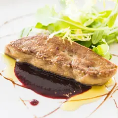 Tranche de foie gras poêlé, joliment assaisonné, servie avec une sauce aux fruits rouges et une salade verte croquante.
