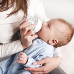 Delikatne karmienie noworodka butelką. Mama trzyma dziecko i podaje mu mleko, pokazując jak karmić noworodka butelką.