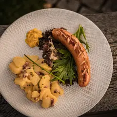 Herzhafter salat zur bratwurst mit Kartoffelsalat, Senf und frischem Grün auf einem Teller.