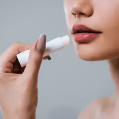 Mano applica balsamo labbra per levigare le rughe, come un codice a barre che scompare.