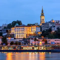 Wieczorny widok na wzgórze z budynkami i kościołem, odbijający się w rzece. Stolica Serbii, Belgrad, prezentuje się malowniczo.