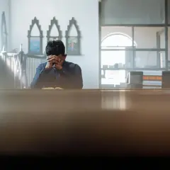 Mężczyzna w kościele pogrążony w głębokiej kontemplacji, z rękami złożonymi na twarzy.