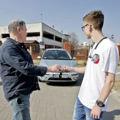 Mężczyźni przekazują sobie kluczyki do samochodu, co symbolizuje umowę użyczenia.