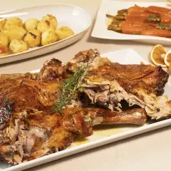 Pierna de cordero lechal al horno jugosa, dorada y tierna, acompañada de patatas asadas y zanahorias glaseadas.