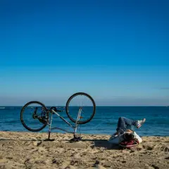 Odpoczynek po przejażdżce Velo Baltica. Rower na plaży, człowiek leży na piasku, patrząc na morze.