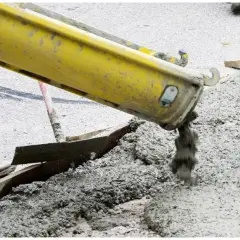 Betoniarka wylewa świeży beton. Pracownicy przygotowują teren, a pytanie "jak długo podlewać beton" jest kluczowe dla jego trwałości.