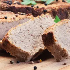 Pokrojony pasztet mieszany drobiowo-wieprzowy, przyprawiony ziarnami pieprzu, na desce.